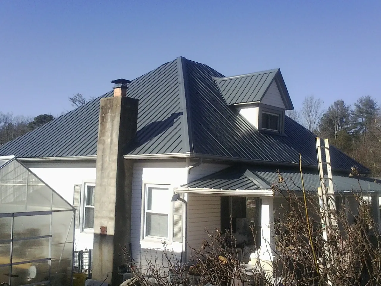 Dark blue standing seam metal roof on a white farmhouse with dormer — Slate & Tile Roof Repair by Roofing Brothers in Coaldale