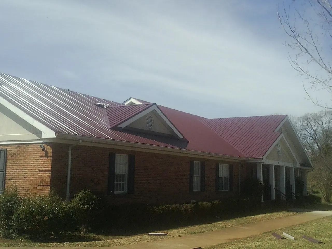 Red metal roof with gabled entries on a long brick building, from a Hail Damage Roof Repair job in Coaldale