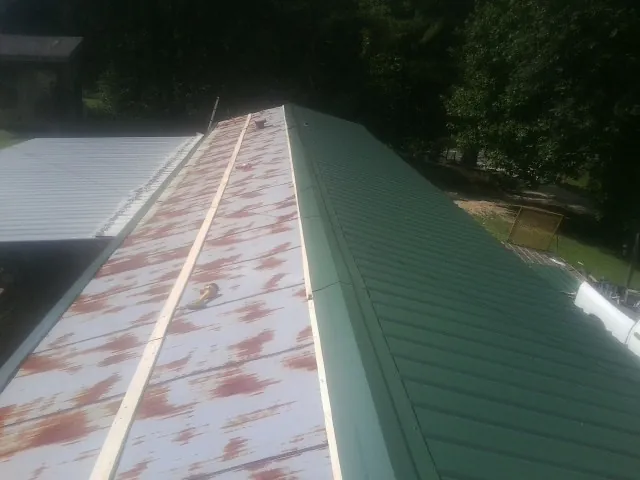 Old rusted panels beside newly installed green metal roofing — Wind Damage Roof Repair by Roofing Brothers in Coaldale