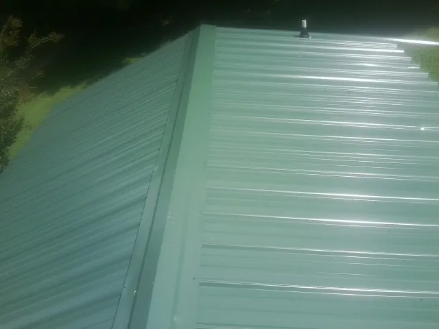 New green metal panels meeting at the ridge of a roof — Flat Roof Repair work by our crew in Coaldale