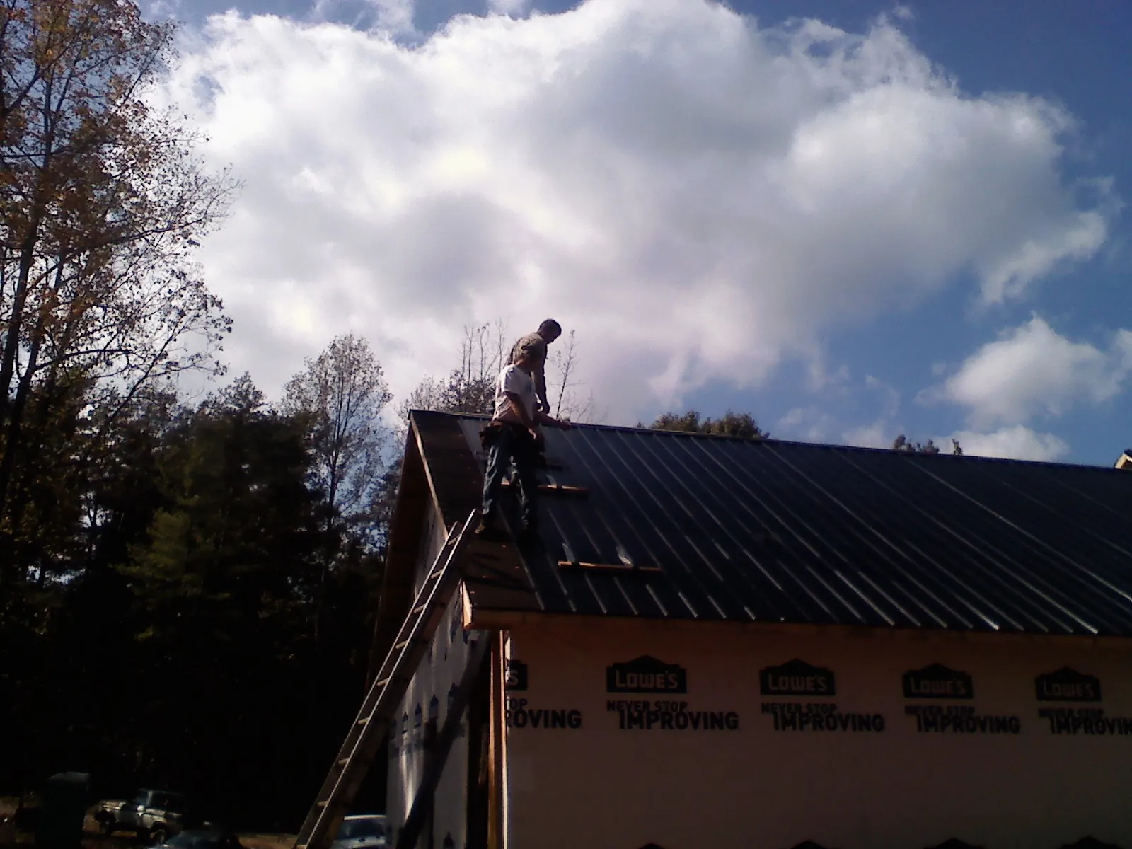 Roofer fastening dark metal panels high against a cloudy sky, from a Roof Inspection job in Coaldale
