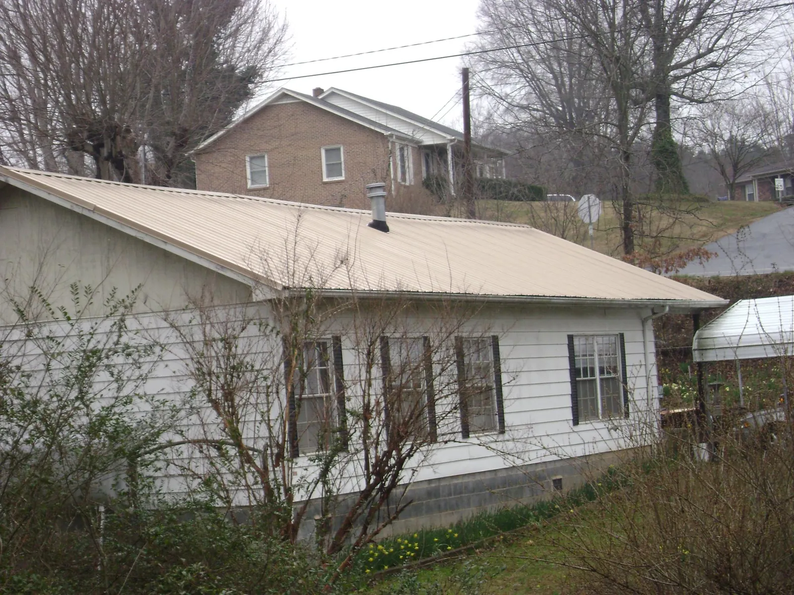 Tan metal roof on a white sided house set into a hillside — Commercial Roofing by Roofing Brothers in Coaldale